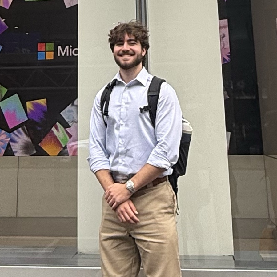Jake smiling in a light blue button-down outside a Microsoft office window